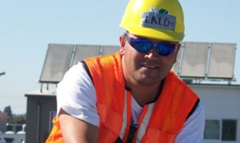 Construction worker wearing yellow hard hat and orange safety vest smiling at camera