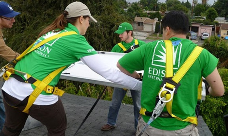 Workers in green EDIS shirts review blueprints on a rooftop during a solar installation project