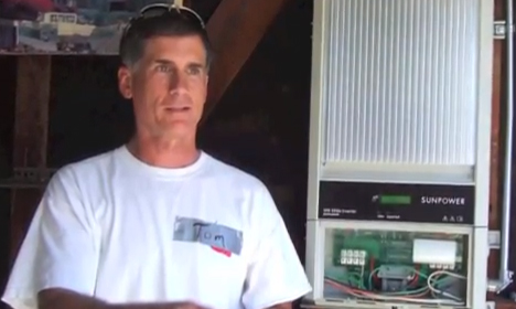 Man in white t-shirt standing next to solar power equipment and control panel indoors