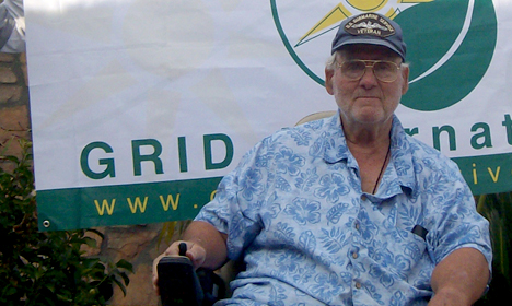 Elmer Rankin wearing glasses and blue patterned shirt stands in front of GRID International banner