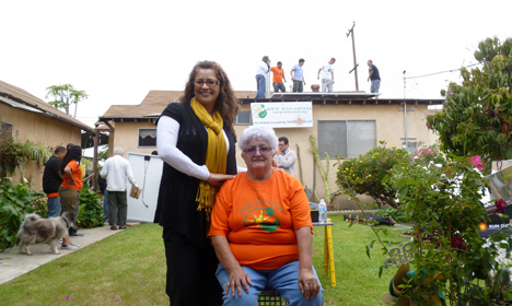 Woman standing behind seated elderly woman in orange shirt at GRID Alternatives solar installation celebration event