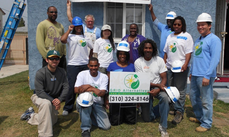 Group of volunteers in white shirts holding a sign for GRID Alternatives with phone number (310) 324-8146 at a community solar installation event