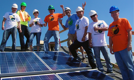 Group of workers in hard hats and safety vests celebrating on a rooftop solar panel installation