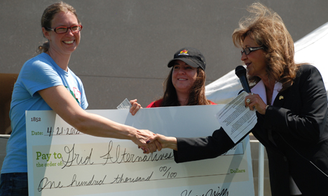 Three women holding a large check for one hundred thousand dollars at an awards ceremony
