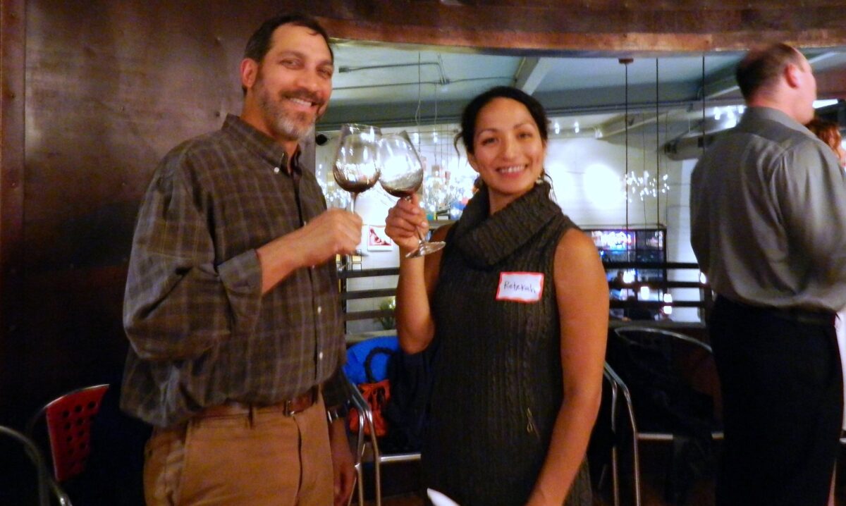 Man and woman toasting wine glasses at a celebration event, wearing name badges