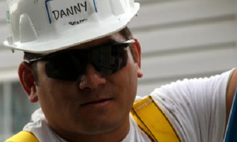 Man wearing white hard hat labeled "DANNY" and yellow safety vest with sunglasses