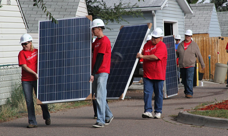 Team in red shirts installing solar panels on residential house roof