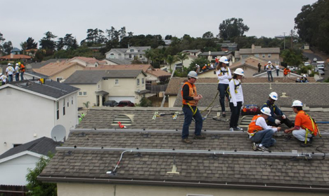 Workers in safety gear installing solar panels on residential rooftops during workforce training program