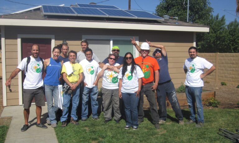 Group of volunteers in matching shirts posing in front of house with solar panels on roof