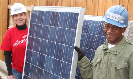 Two workers in hard hats installing solar panels on wooden structure