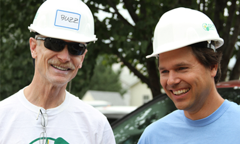 Two smiling men wearing white hard hats and safety gear outdoors