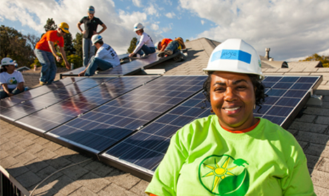 Solar installer in green shirt smiling at camera during rooftop solar panel installation event in South LA
