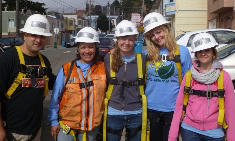 Five construction workers in hard hats and safety vests smiling outdoors in a residential neighborhood
