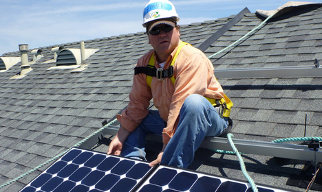 Roofer in safety gear installing solar panel on residential rooftop