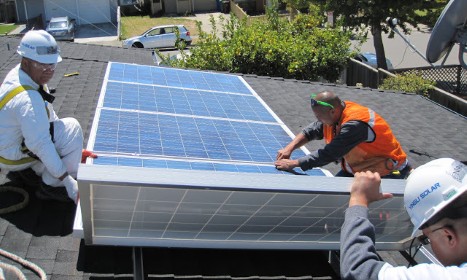 Three workers in hard hats installing a solar panel on a residential roof during a hands-on training