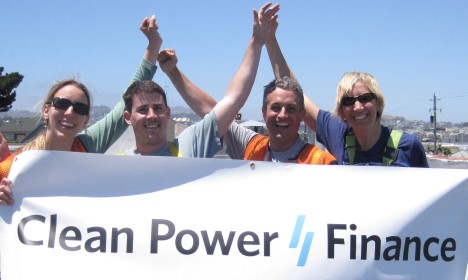 Four people raising joined hands while holding a Clean Power Finance banner outdoors