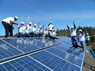Group of volunteers celebrate on rooftop with solar panels installed on residential home