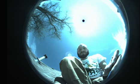Person viewed through fisheye lens looking up at bright sky with bare tree branch visible