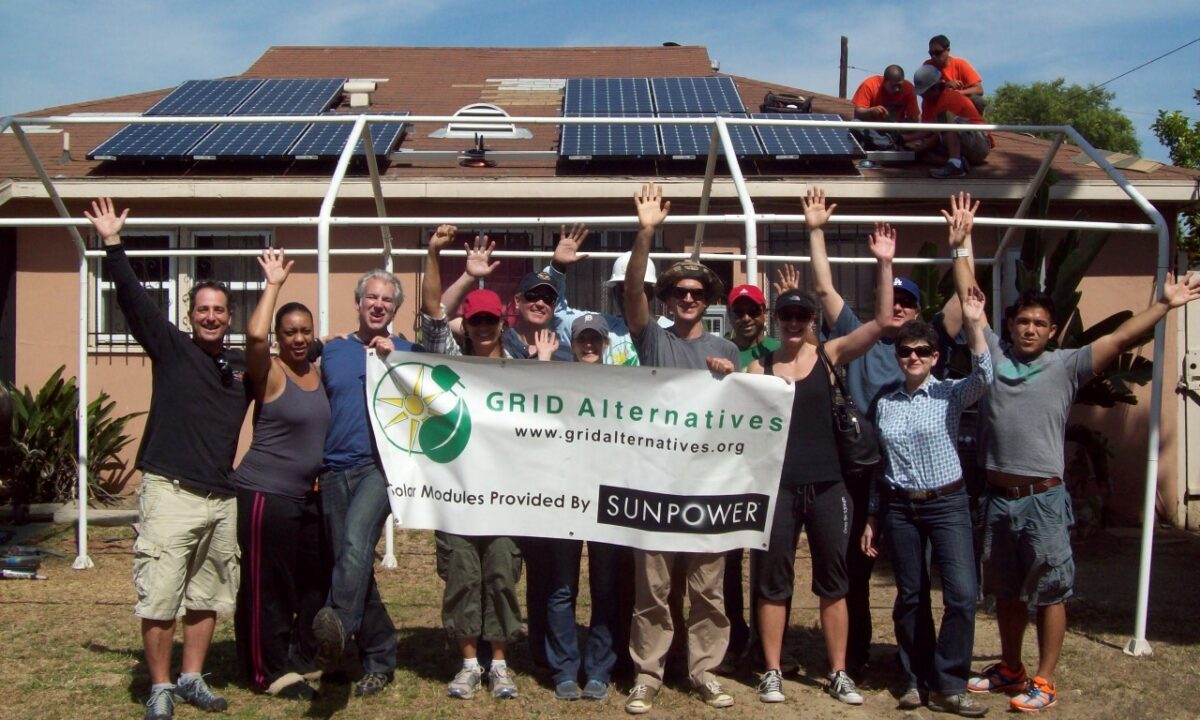 Group holding GRID Alternatives banner in front of house with solar panels on roof