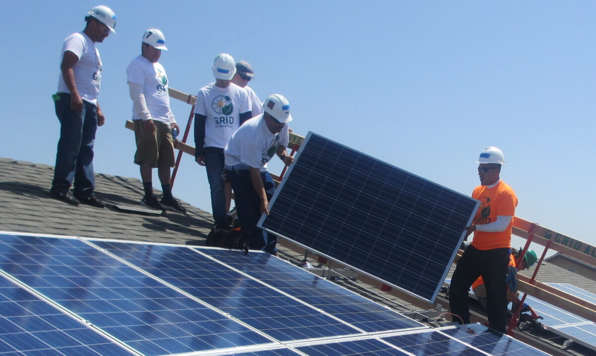 Workers in hard hats install solar panels on a rooftop during job training