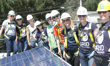 Group of workers in hard hats and safety vests examining solar panels on a roof