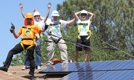Four people celebrate on solar panels during a Solarthon event promoting renewable energy