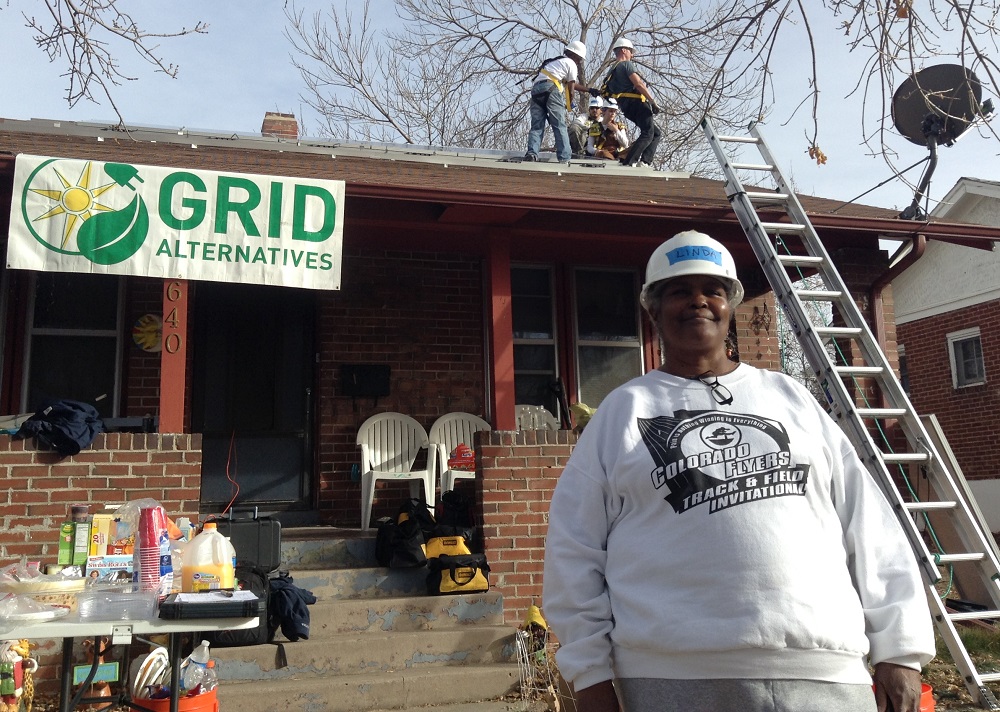 Worker in white hard hat smiles while colleagues install solar panels on GRID Alternatives community building