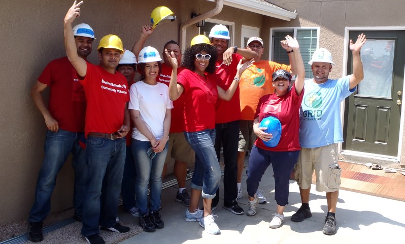 Bank of America volunteers in hard hats and red shirts pose together during a solar installation project in Clovis