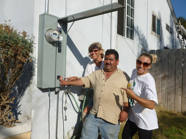 Three people examining an electrical meter on a white building exterior wall