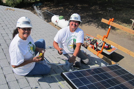 Two volunteers in hard hats install solar panels on a roof for the Bishop Paiute Tribe community project