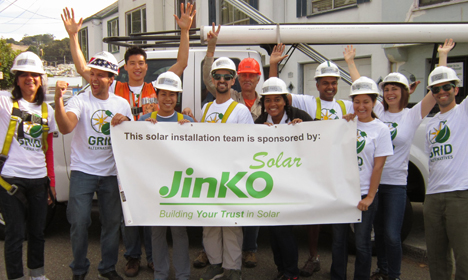 Solar installation team in hard hats holding Jinko Solar banner with arms raised