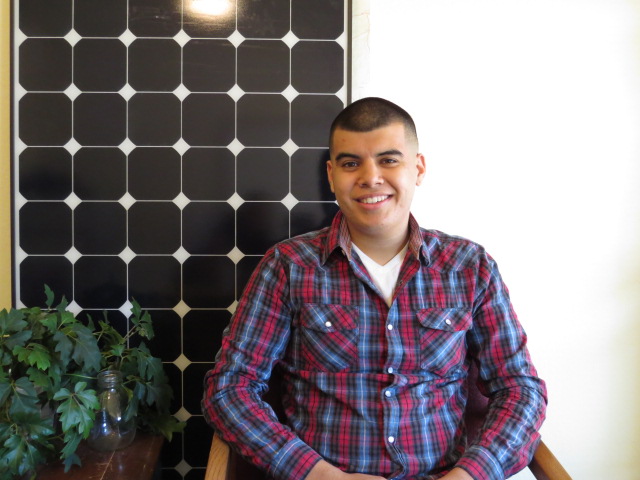 Young man in plaid shirt smiling in front of solar panel display