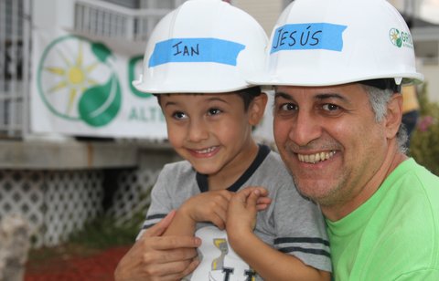 Adult and child wearing hard hats labeled "Jesus" and "Ian" at a community rebuilding project in Far Rockaway