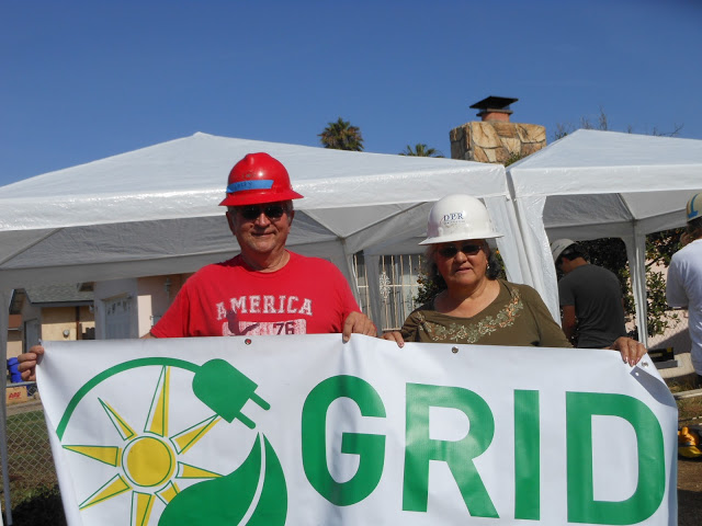 Two people holding a SGRID banner with sun logo at outdoor event under white tent