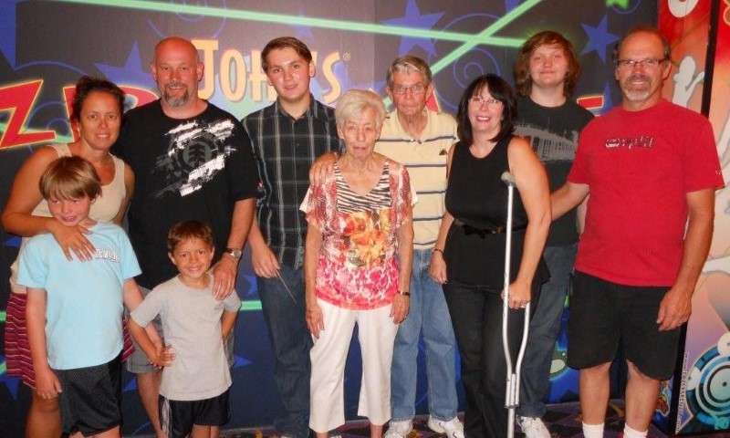 Large multi-generational family group posing together at an event venue with colorful signage behind them