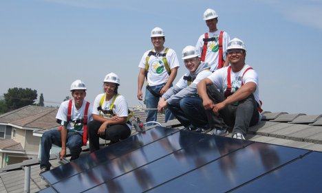 Team of workers in hard hats posing on residential rooftop with solar panels installed