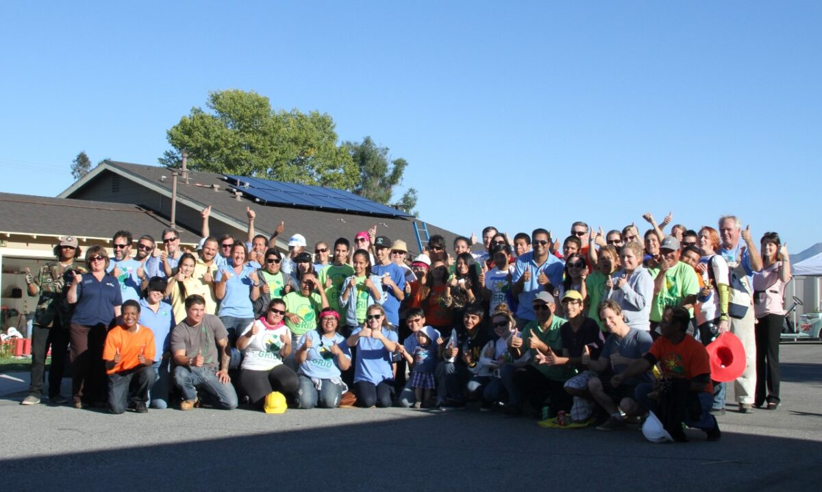 Large group of people cheering with arms raised in front of a building with solar panels during GRID IE 2013 Solarthon event