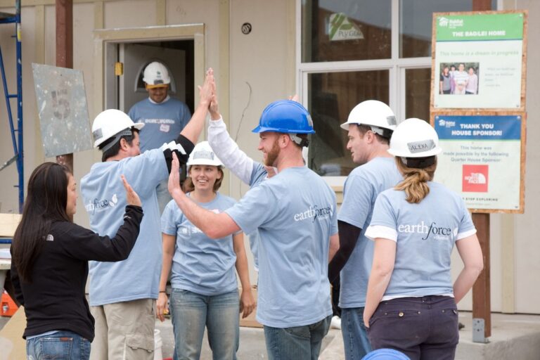 Volunteers in hard hats and earthforce t-shirts high-five during a home construction or renovation project