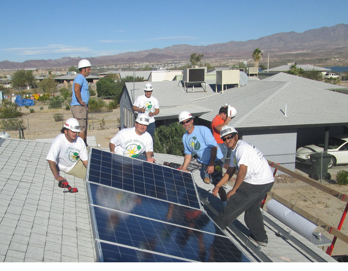 Construction workers installing solar panels on a residential rooftop with mountains in background