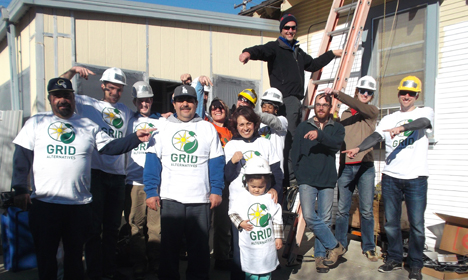 Group of volunteers in GRID t-shirts and hard hats at a construction site, smiling and celebrating together