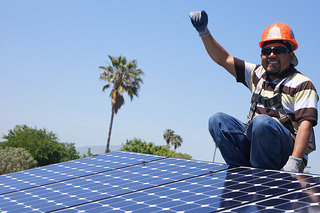 Worker in orange hard hat waving while installing solar panels on roof