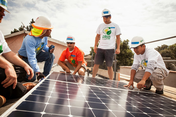 Team installing solar panels on rooftop, wearing hard hats and safety gear