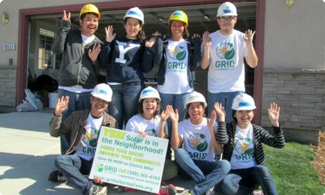 Group of volunteers in hard hats and GRID shirts holding sign about neighborhood solar initiative