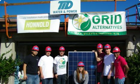 Team wearing pink hard hats holding solar panel at TP Water & Power, Honnold, and Grid Alternatives event