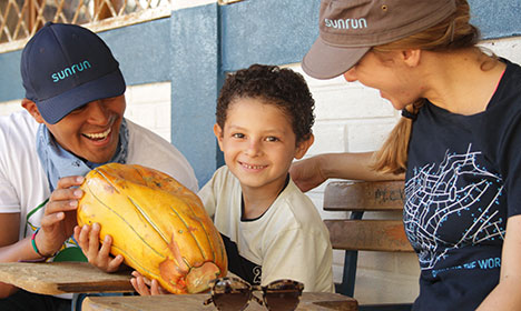Two adults and a child smile while holding a large yellow cacao pod outdoors