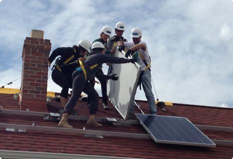 Workers installing solar panels on a residential roof with hard hats and safety equipment