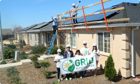 Team members holding GRID Alternatives banner in front of house with solar panels being installed on roof