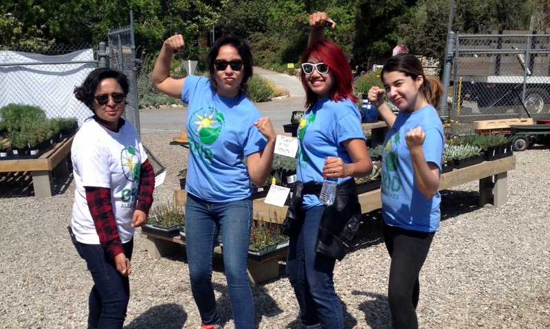 Four volunteers in blue SolarCorps shirts pose with fists raised at a community garden event honoring Cesar Chavez