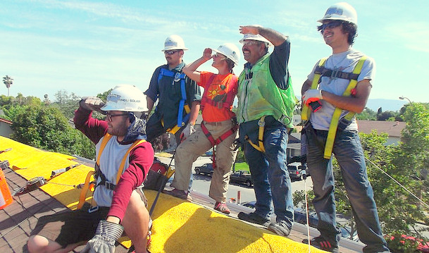 Group of workers in hard hats and safety vests installing solar panels on a roof