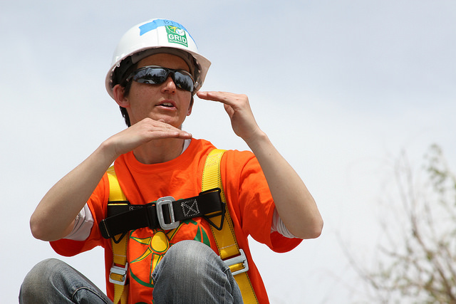 Construction worker in safety gear and hard hat adjusting sunglasses while crouching outdoors